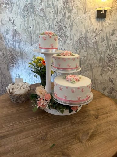 Bespoke Three-tier Floral Wedding Cake A three tier white fondant wedding cake on a white stand with hand crafted sugar flowers, pink daisies, peonies and roses in Bedfordshire